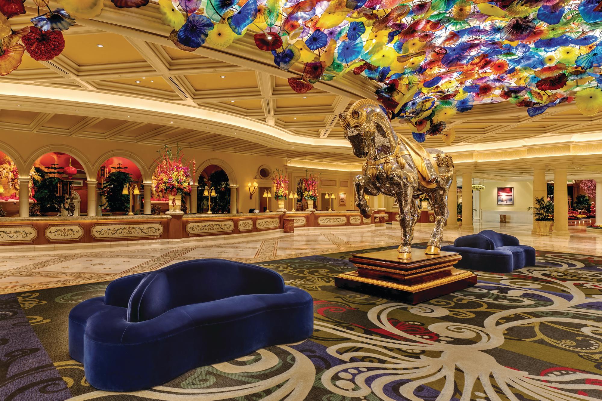 Reception of the Bellagio with desks, a gold horse statue, blues velvet couches and ceiling full of colorful umbrellas made of glass.