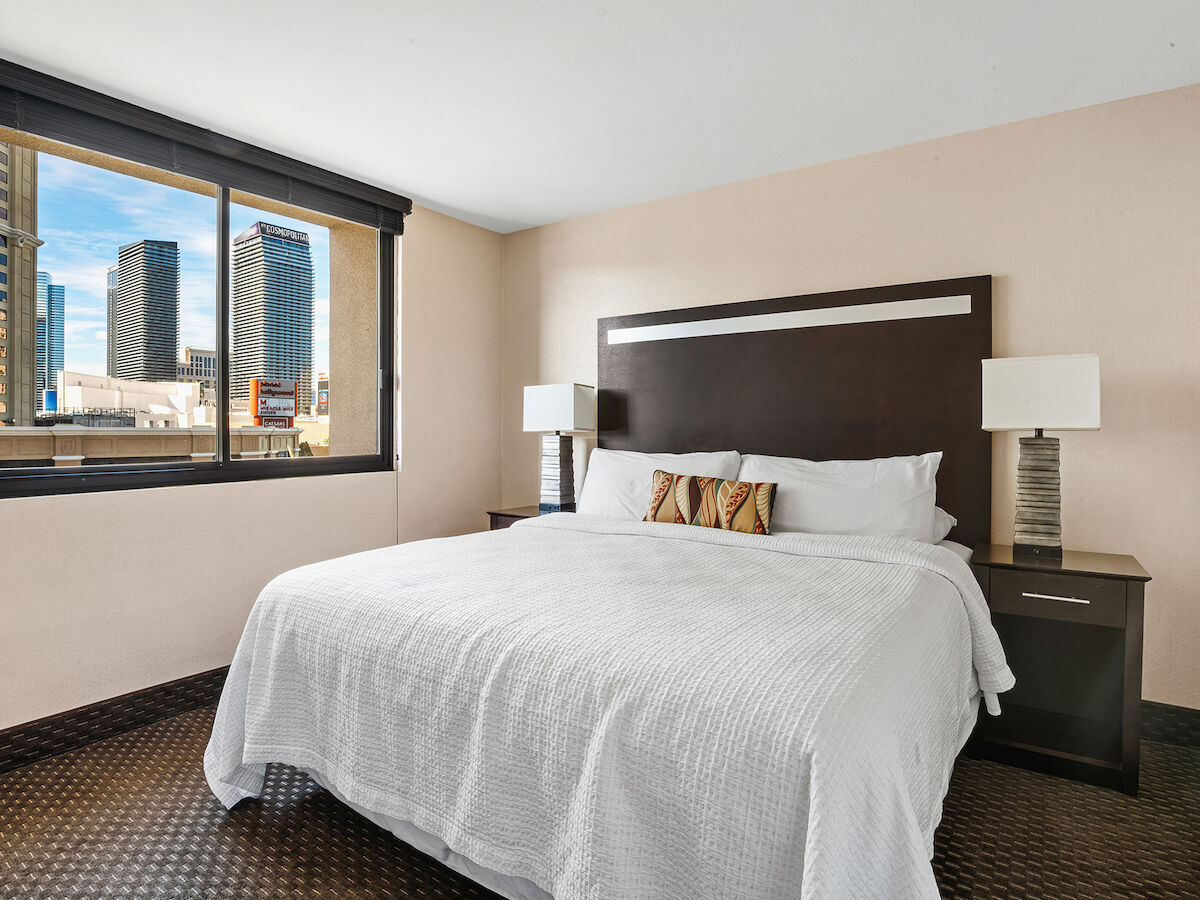 A modern hotel room with a large bed, two side tables with lamps, and a window offering a view of city skyscrapers ends the sentence.