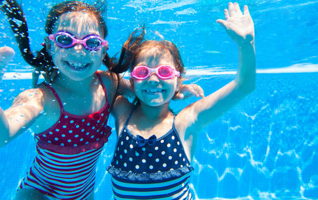 Two young girls happily playing underwater in a swimming pool, showcasing the pool's amenities amenities