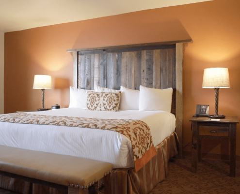 A hotel room with a king-size bed and two nightstands. Each nightstand has a lamp, with one also featuring a telephone and the other a clock.