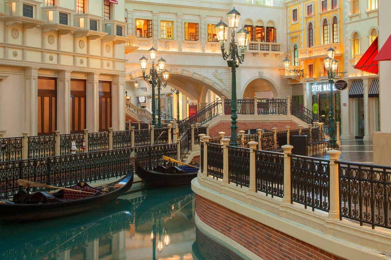 Interior of a Venetian-themed shopping mall with gondolas on a canal, ornate lampposts, and facades resembling Venice buildings. Indoor Gondolas